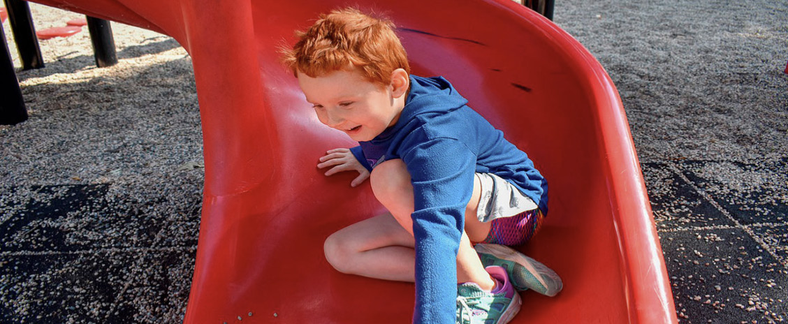 A young child climbing through a red slide on the speedway playground